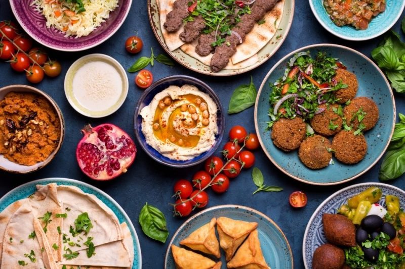 Flat lay of a Middle Eastern food spread featuring falafel, hummus, kebabs, and various dips garnished with fresh tomatoes and pomegranate.